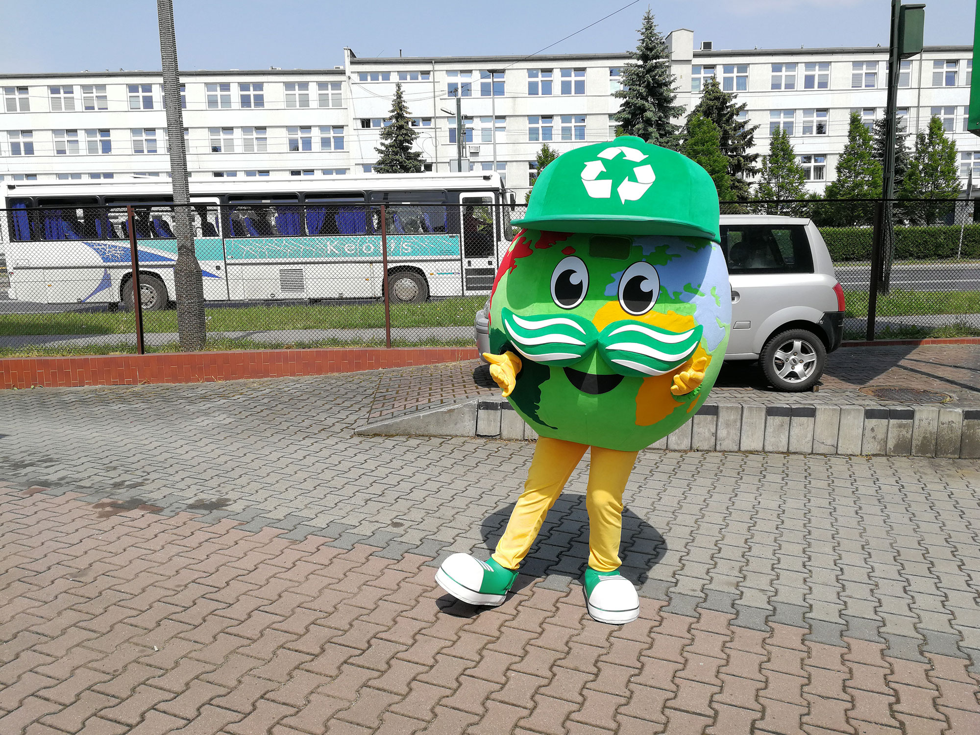 Na fotografii widnieje kostium reklamowy w postaci globusa pozujący do zdjęcia przed siedzibą firmy Elabika